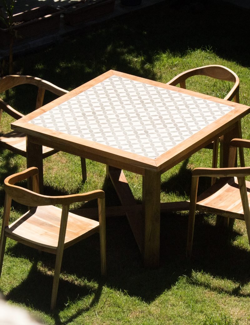 Custom teak dining table with patterned tile top and matching chairs on a garden lawn in Bali